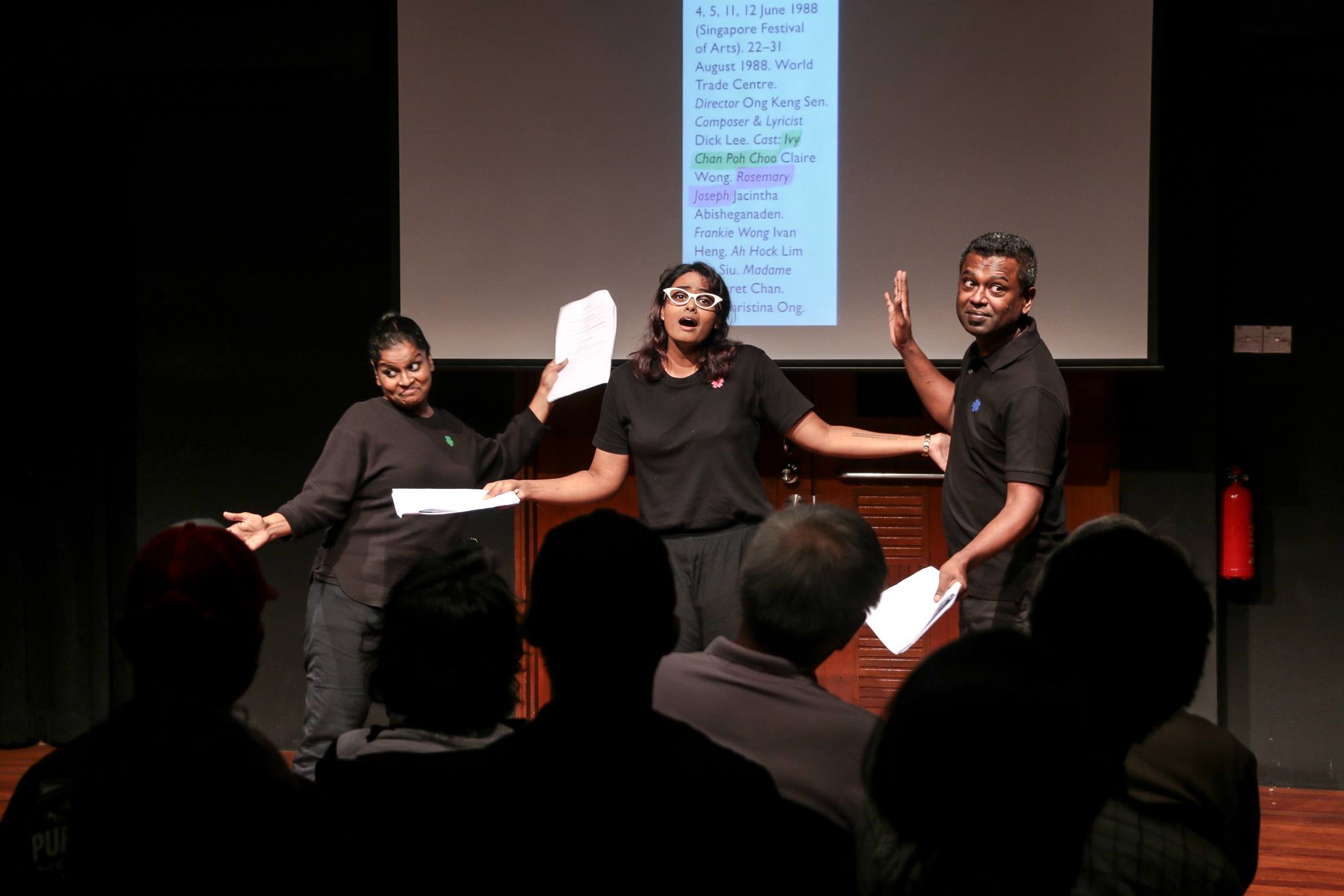Three actors performing a dramatic scene, with scripts in their hands.