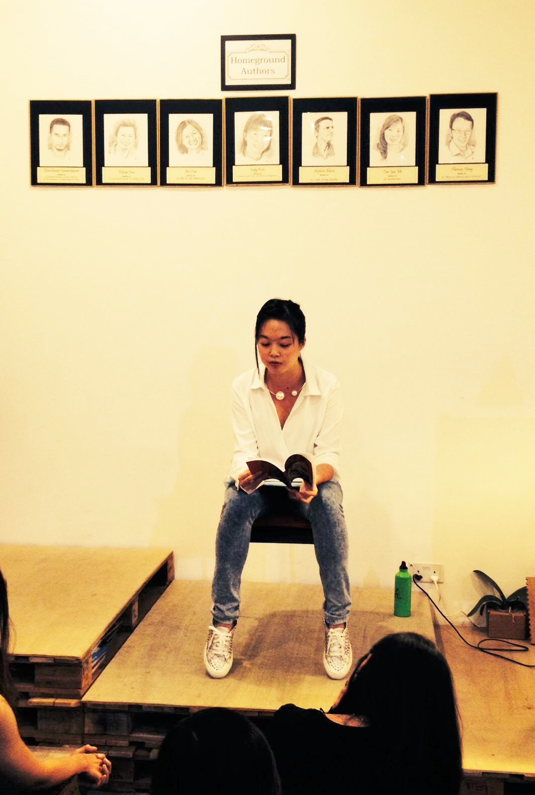 Euginia Tan in a white blouse and jeans, presenting her writing at a sharing. Euginia Tan in a white blouse and jeans, presenting her writing at a sharing.