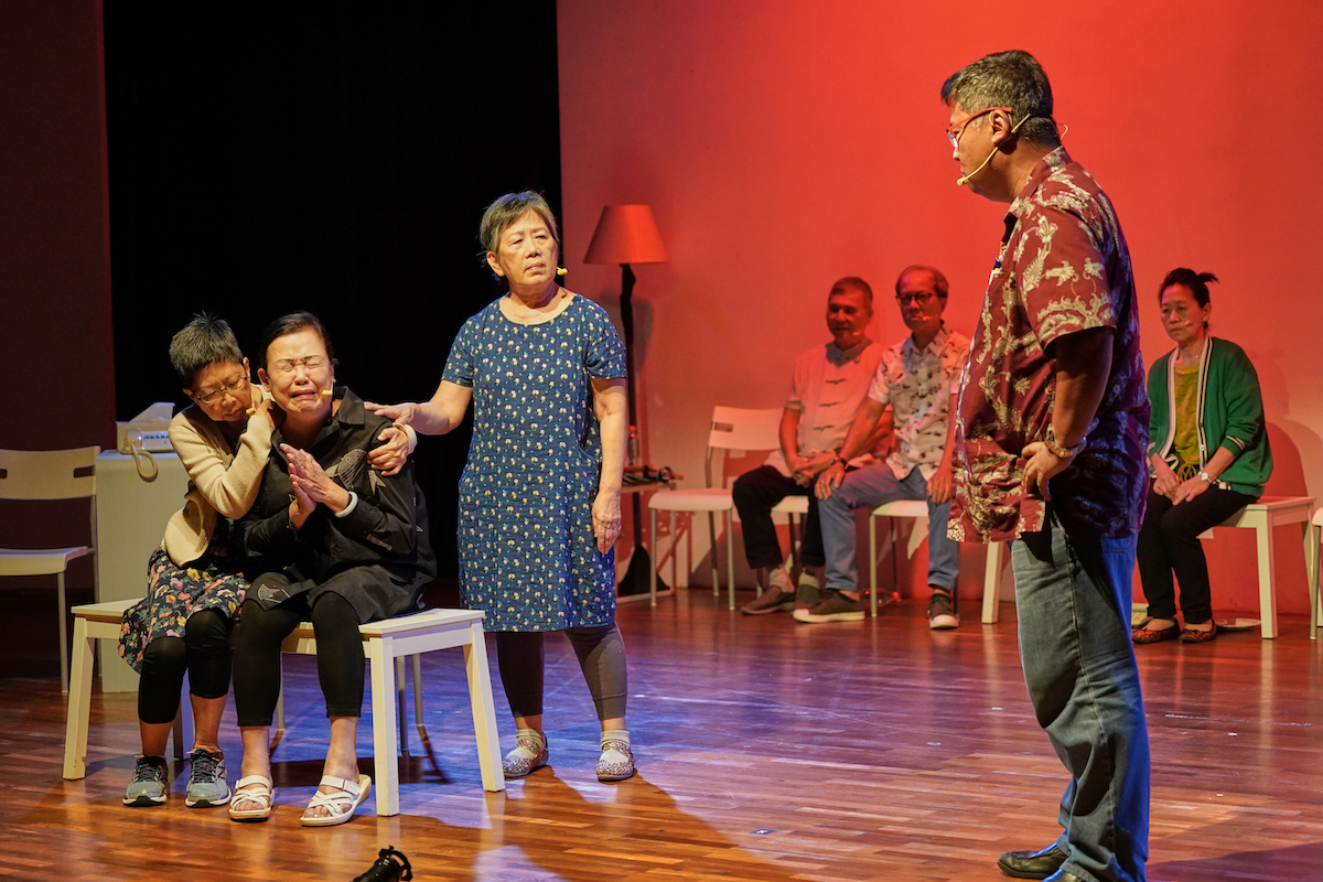 A female-presenting person crying on a bench. Two others attempt to comfort her while a male-presenting person stares at her with his hands on his hips.