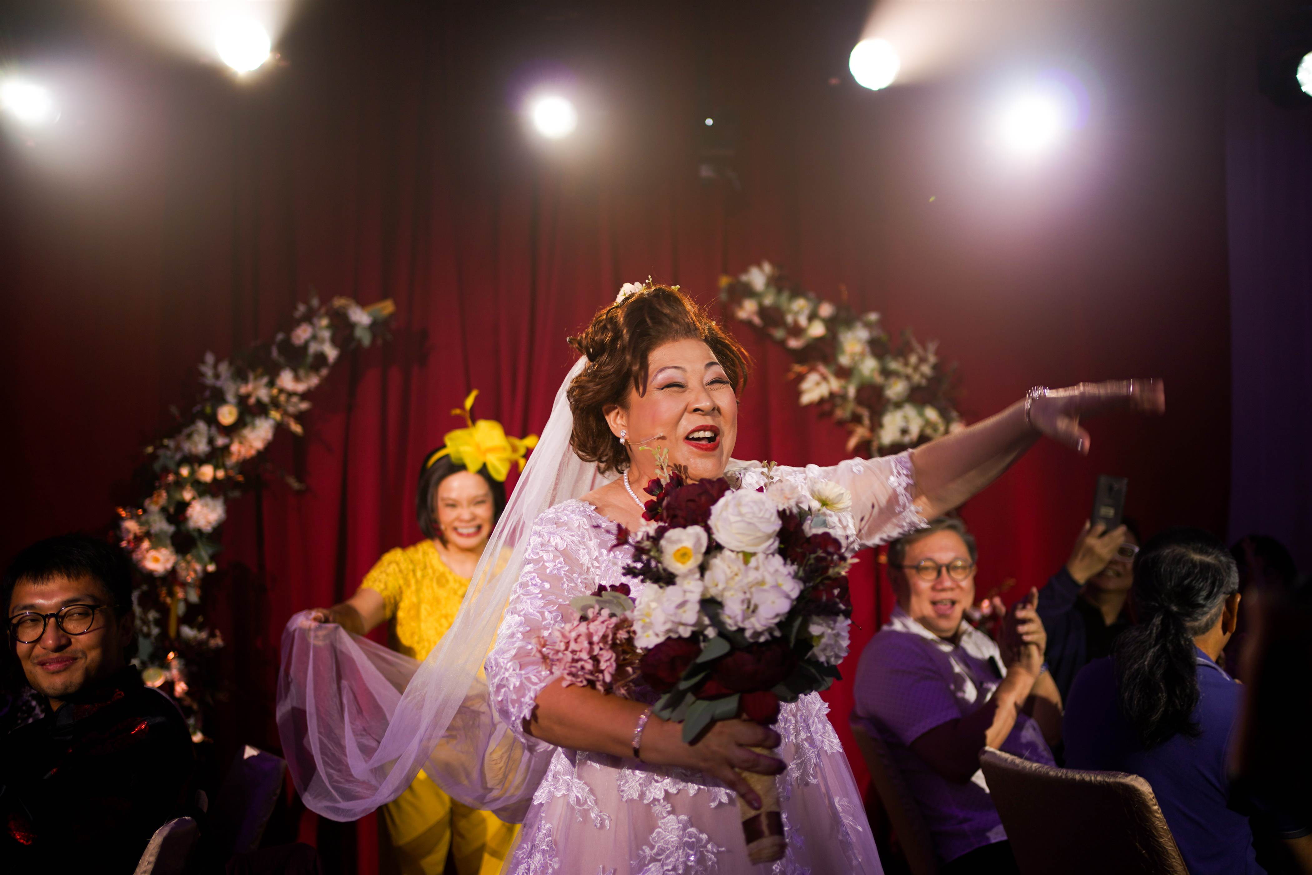 A female character dressed in bridal attire, holding a bouquet, walks down the aisle.