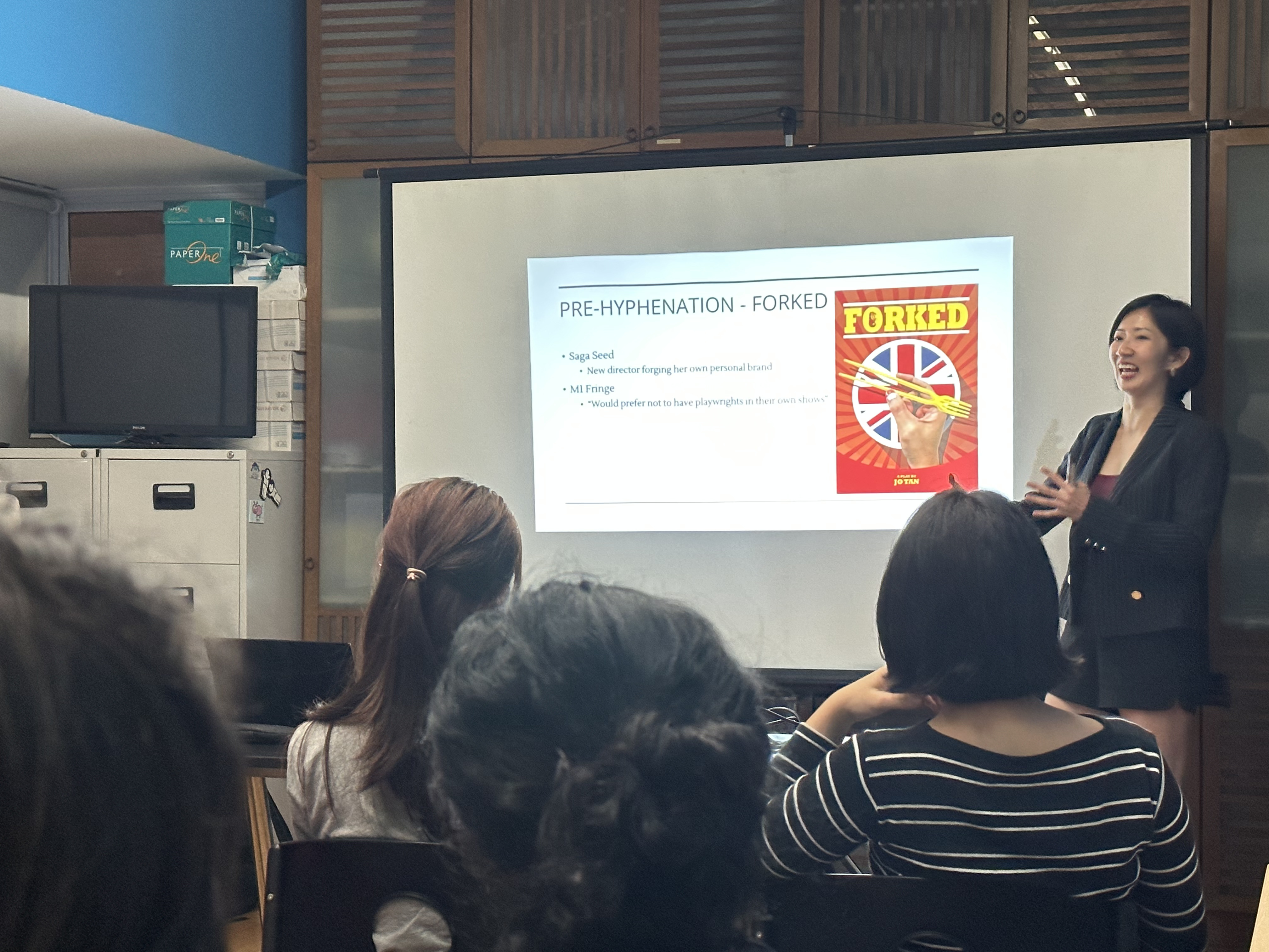 A photograph of Jo standing next to a slide that says "Pre-Hyphenation - Forked".