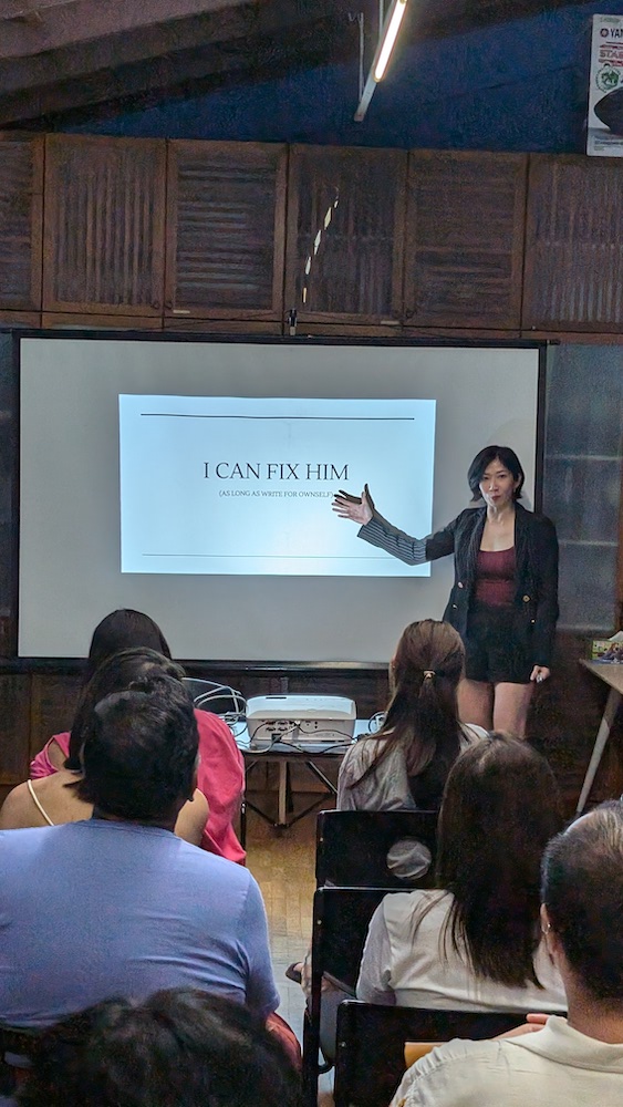 A female-presenting person gesturing at a screen to an audience of people.
