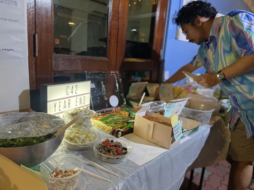 A long table filled with different kinds of food. A person leans over the table to take some food.