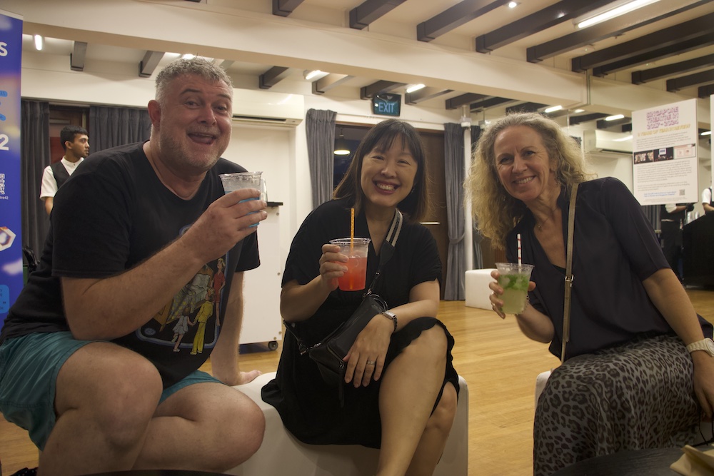 Three persons seated together, holding plastic cups of drinks and smiling.