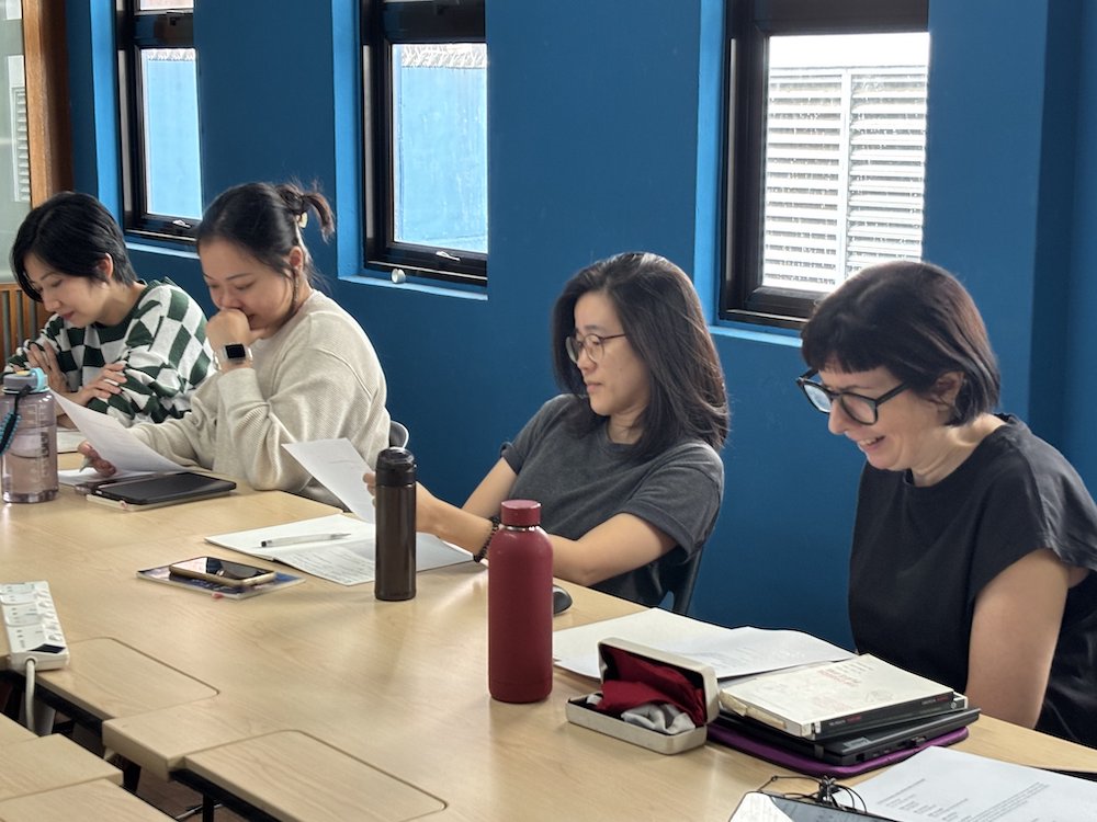 Four persons seated at a table. Two read off scripts in front of them.