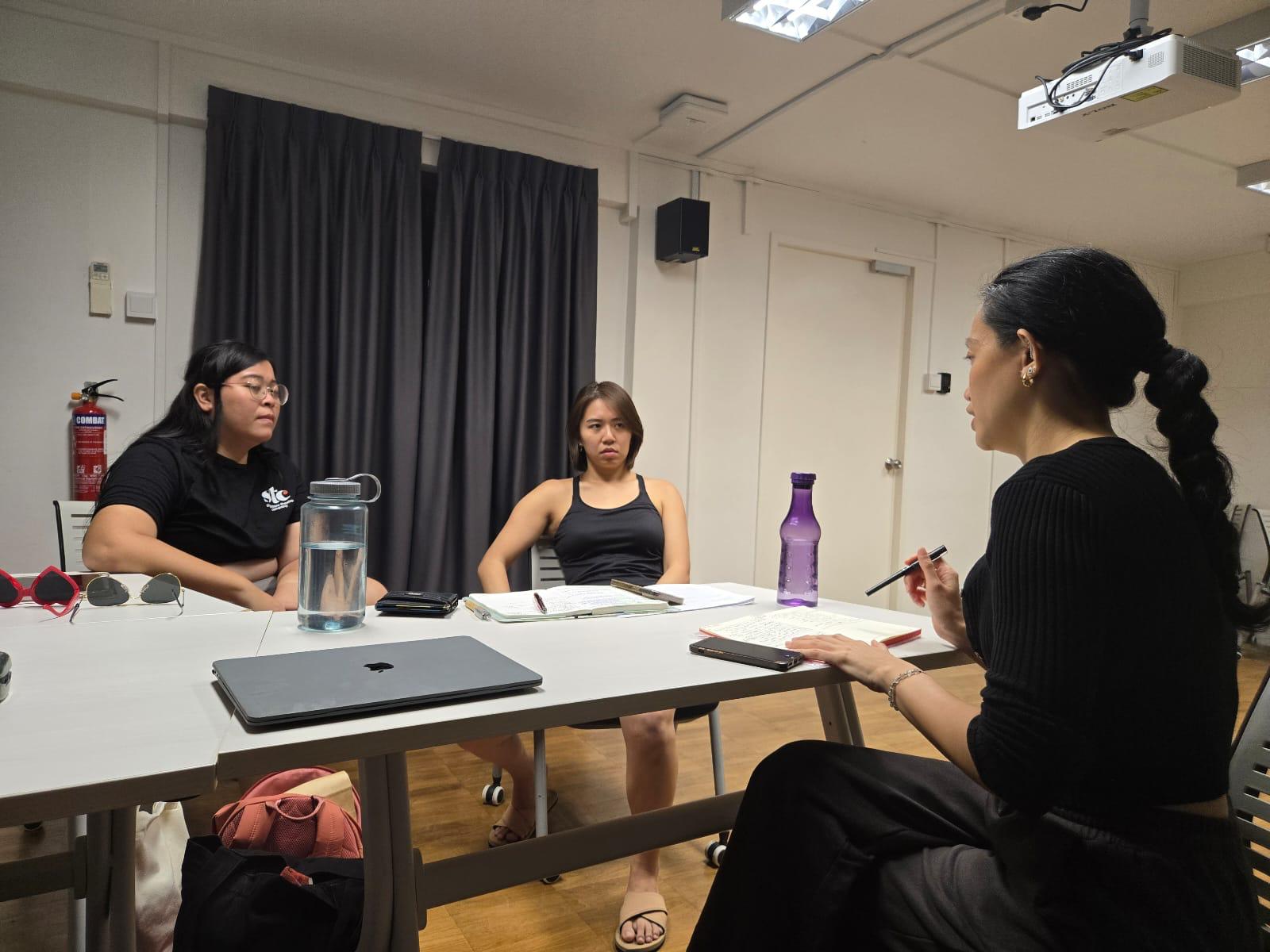 A photograph of three female-presenting people seated around a table.