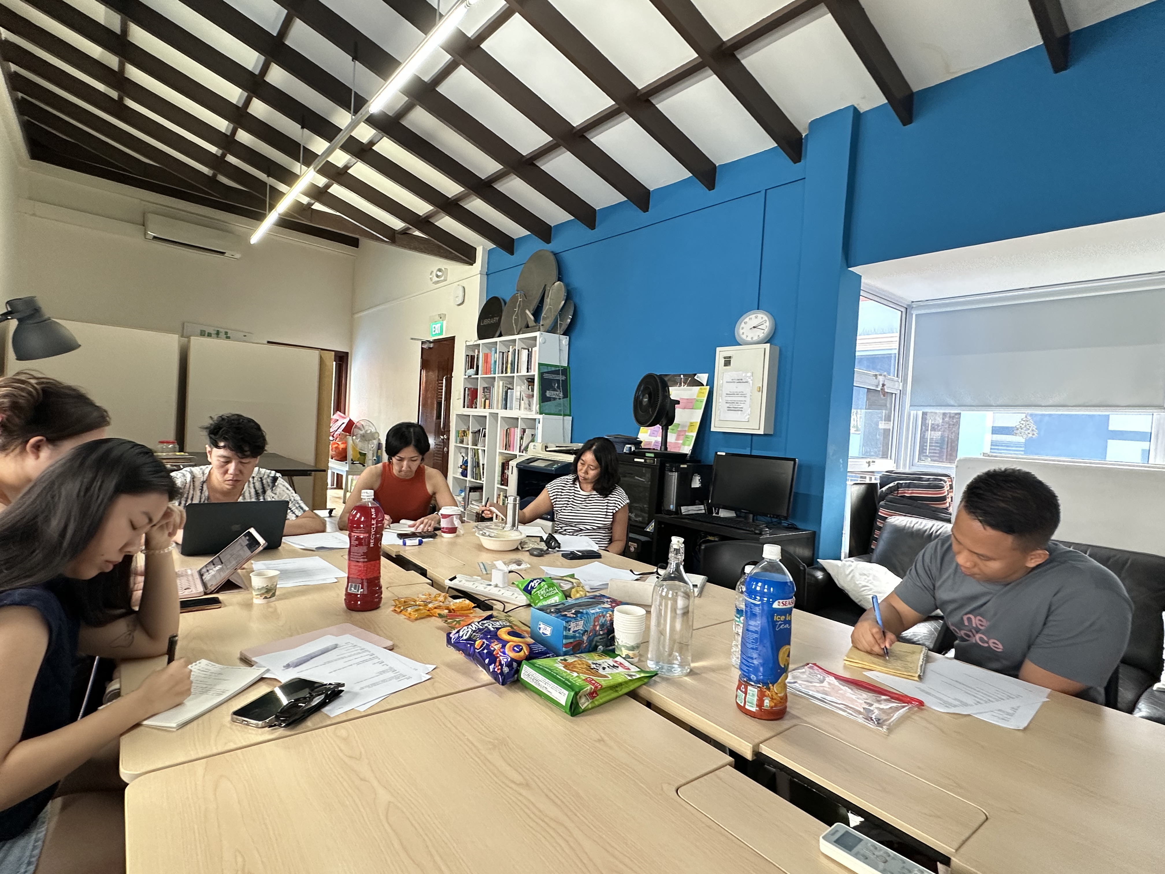 Participants seated around tables and writing on notebooks.
