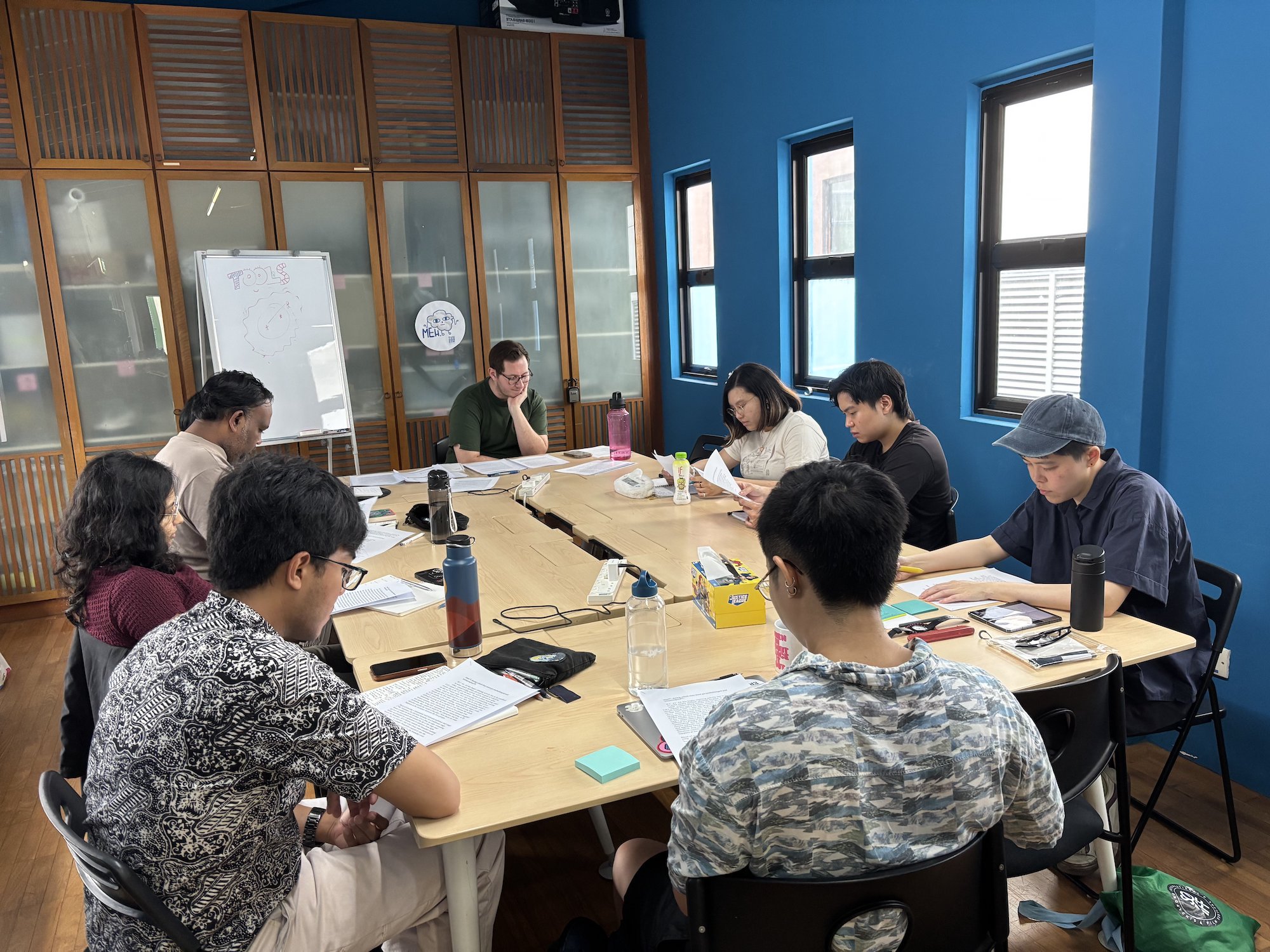 A group of people seated around tables, reading from papers.