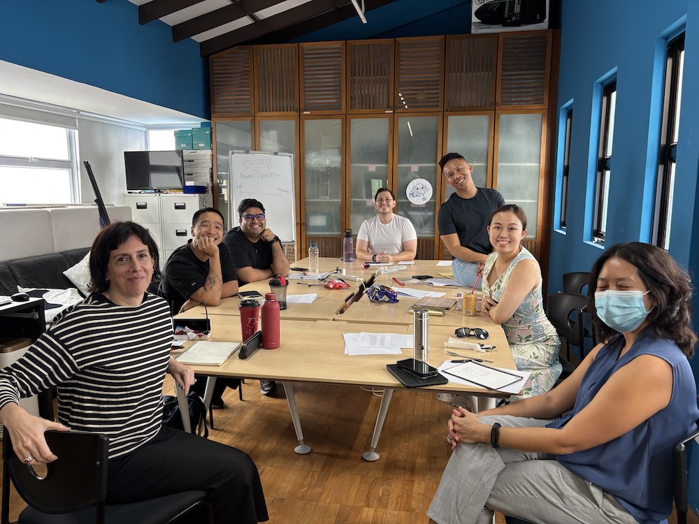 Seven people seated around tables, smiling into the camera.