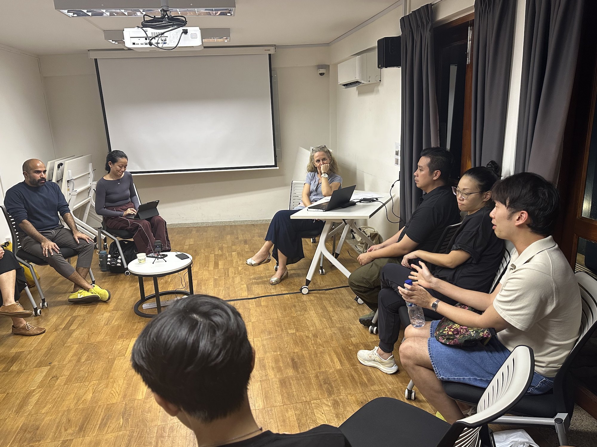 A few persons seated along a wall, speaking to other persons facing them. A few persons seated along a wall, speaking to other persons facing them.