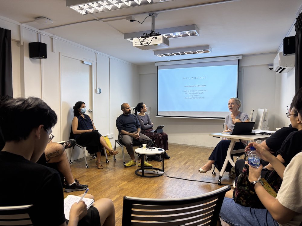 A wide-angle view of four persons seated in the front of a room, looking at a projector screen. A wide-angle view of four persons seated in the front of a room, looking at a projector screen.