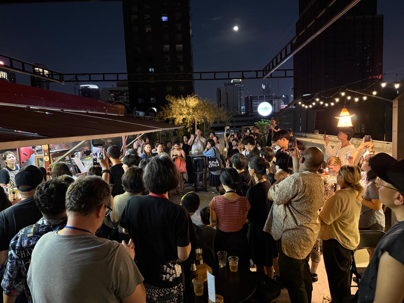 A large group of people on a brightly lit rooftop, under the night sky. A large group of people on a brightly lit rooftop, under the night sky.