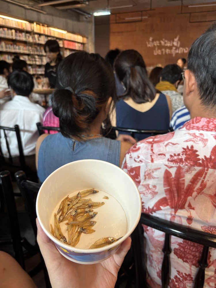 A small bowl with some tiny fish. In the background is an audience to a performance. A small bowl with some tiny fish. In the background is an audience to a performance.