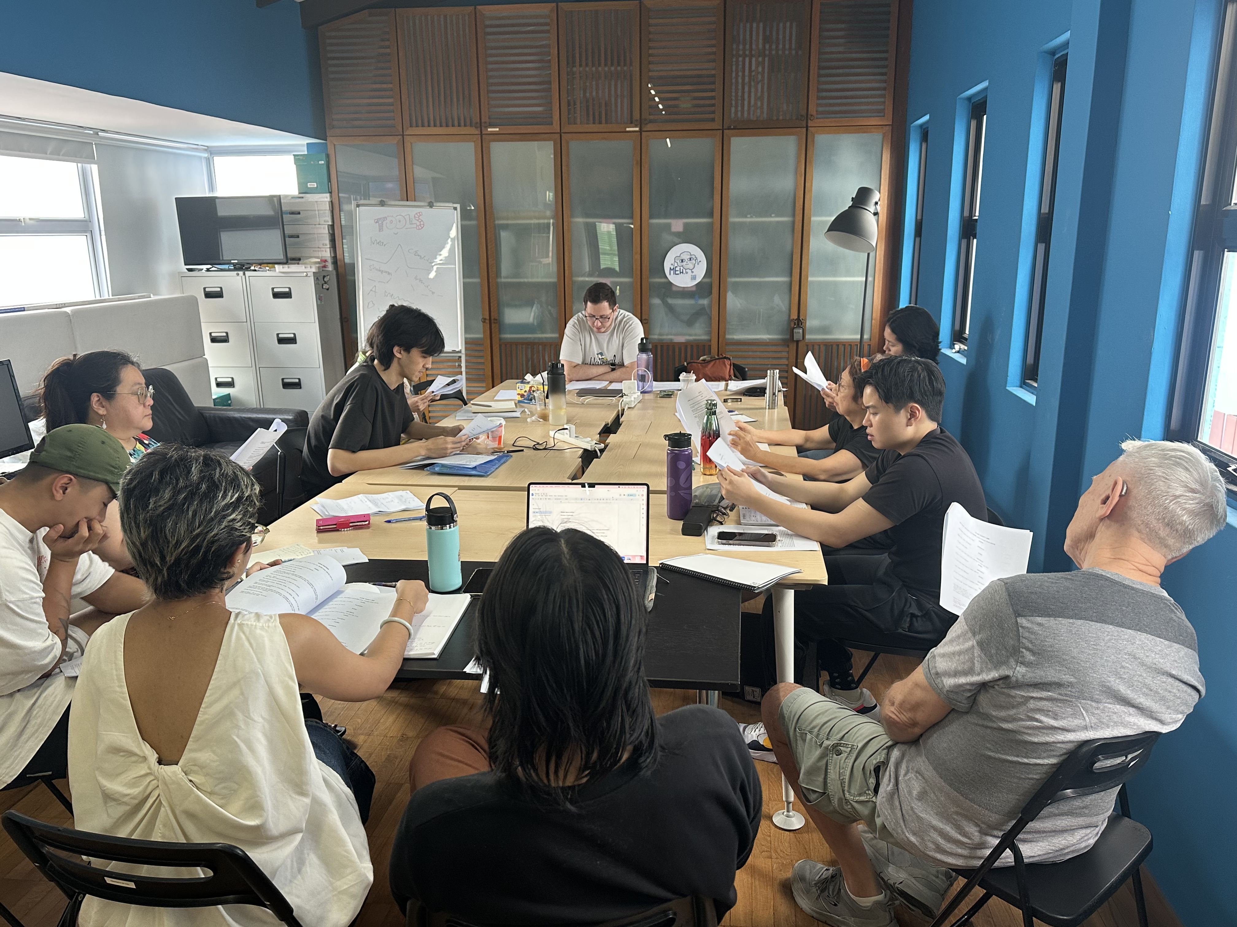 Participants seated around tables reading from scripts in hand.