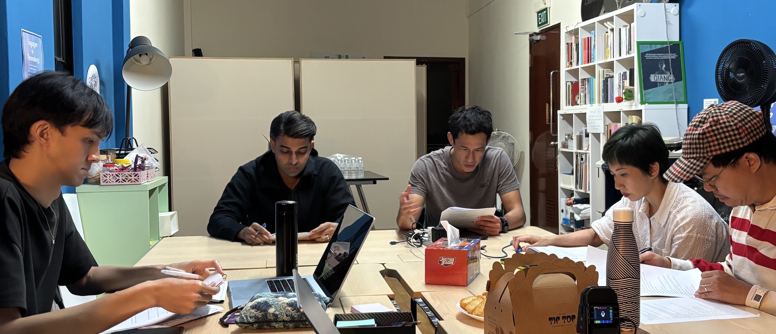 Five people seated around a table, focusing intently on the scripts in front of them. Five people seated around a table, focusing intently on the scripts in front of them.