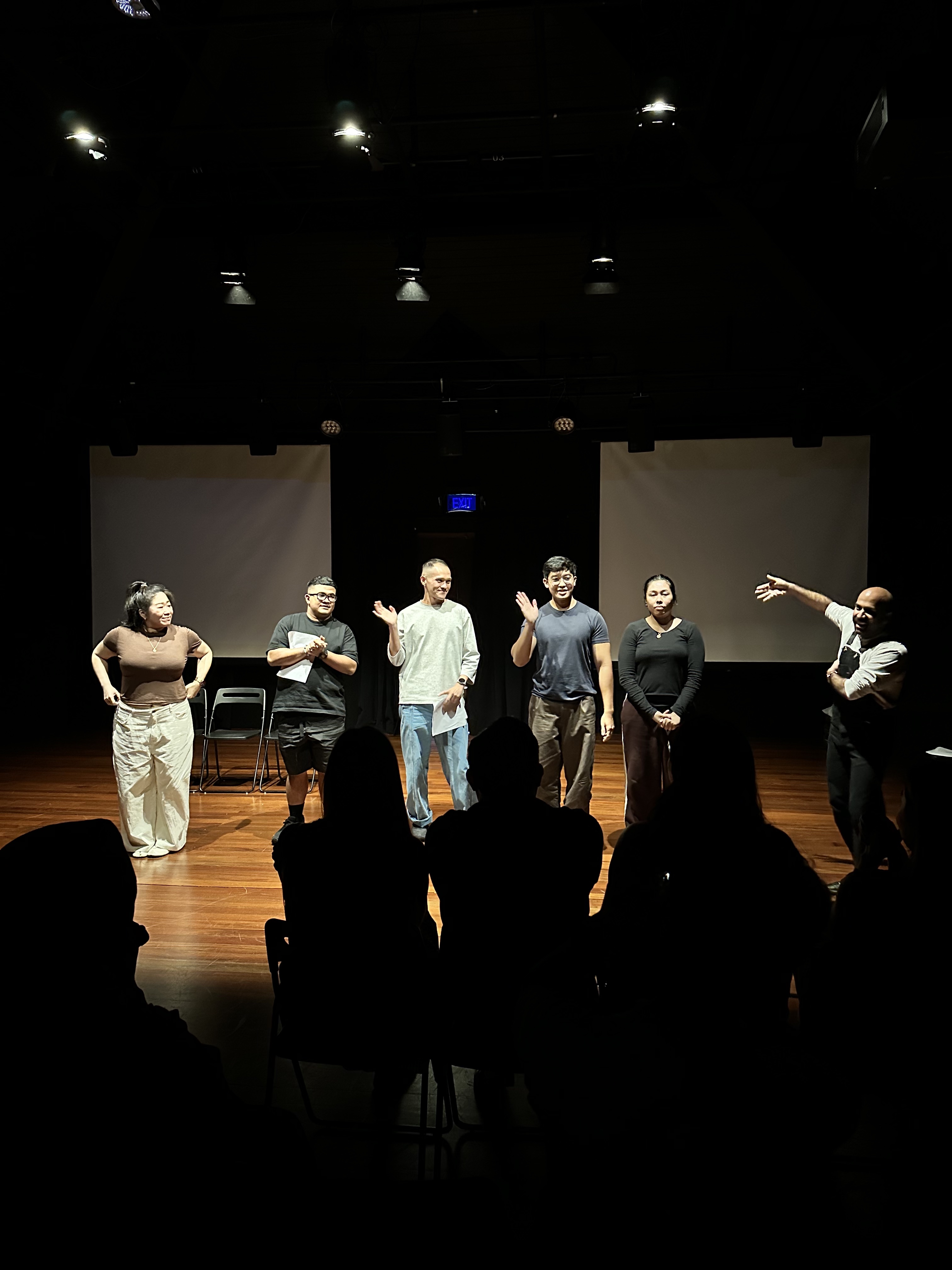 A male-presenting person gestures enthusiastically at five people standing in a row. A male-presenting person gestures enthusiastically at five people standing in a row.