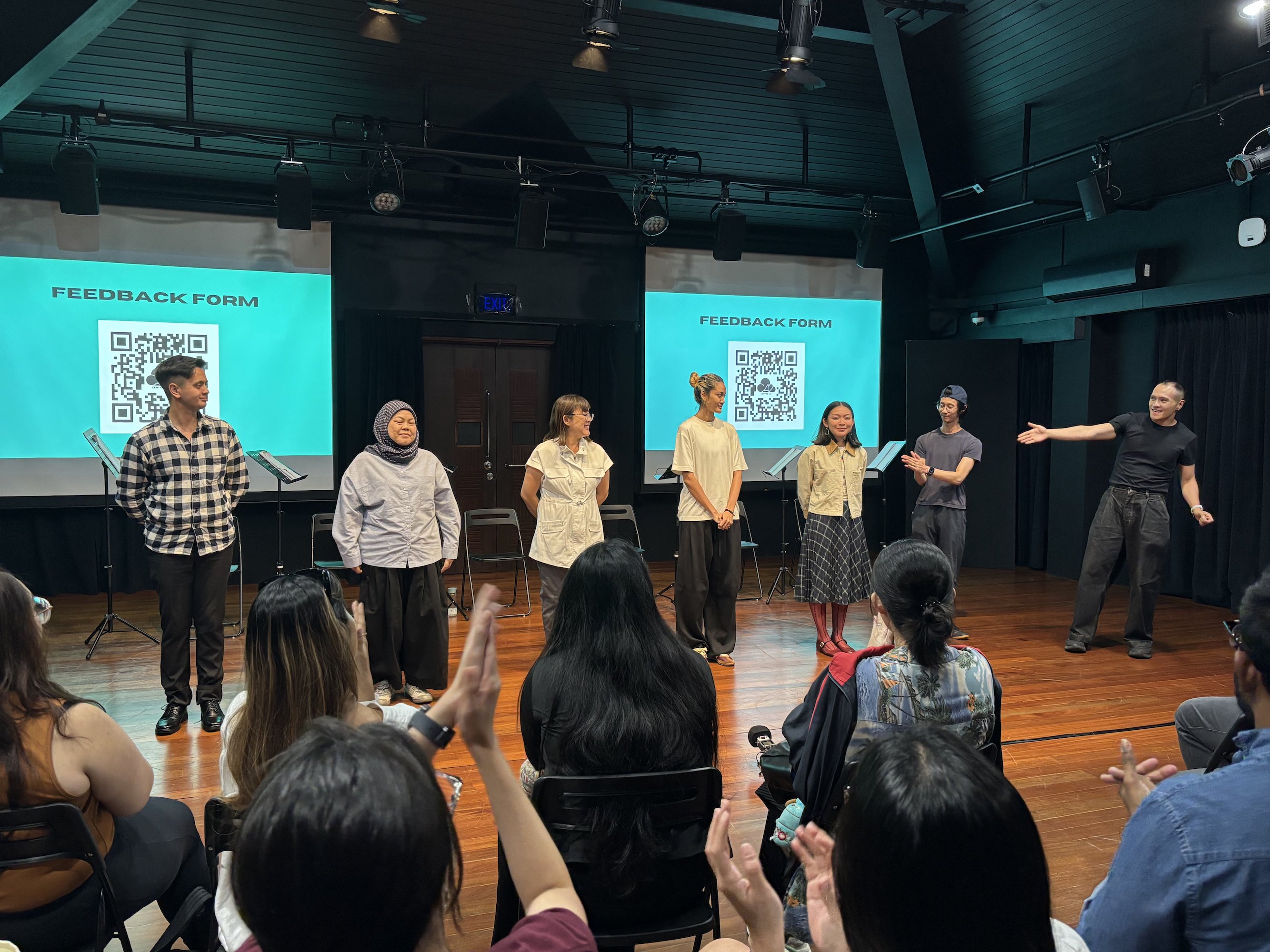 A male-presenting person gestures enthusiastically at six people standing in a row.