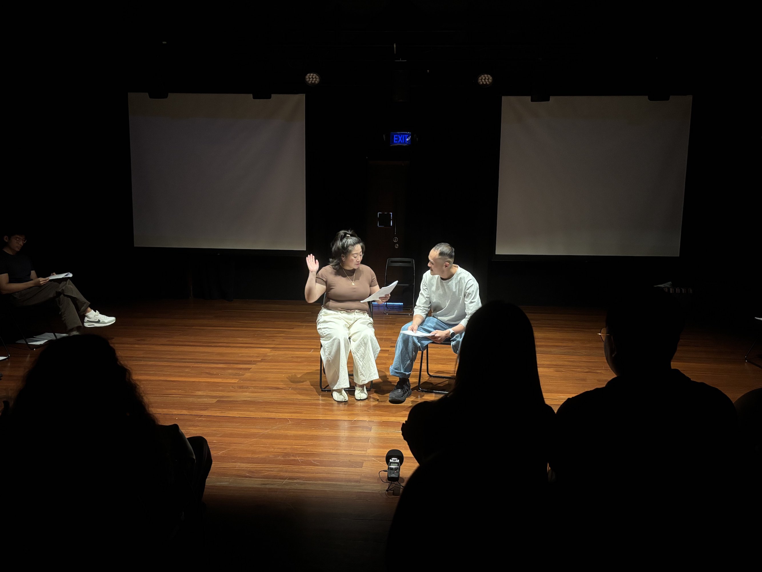 Two persons seated side by side in chairs in a black box. Two persons seated side by side in chairs in a black box.