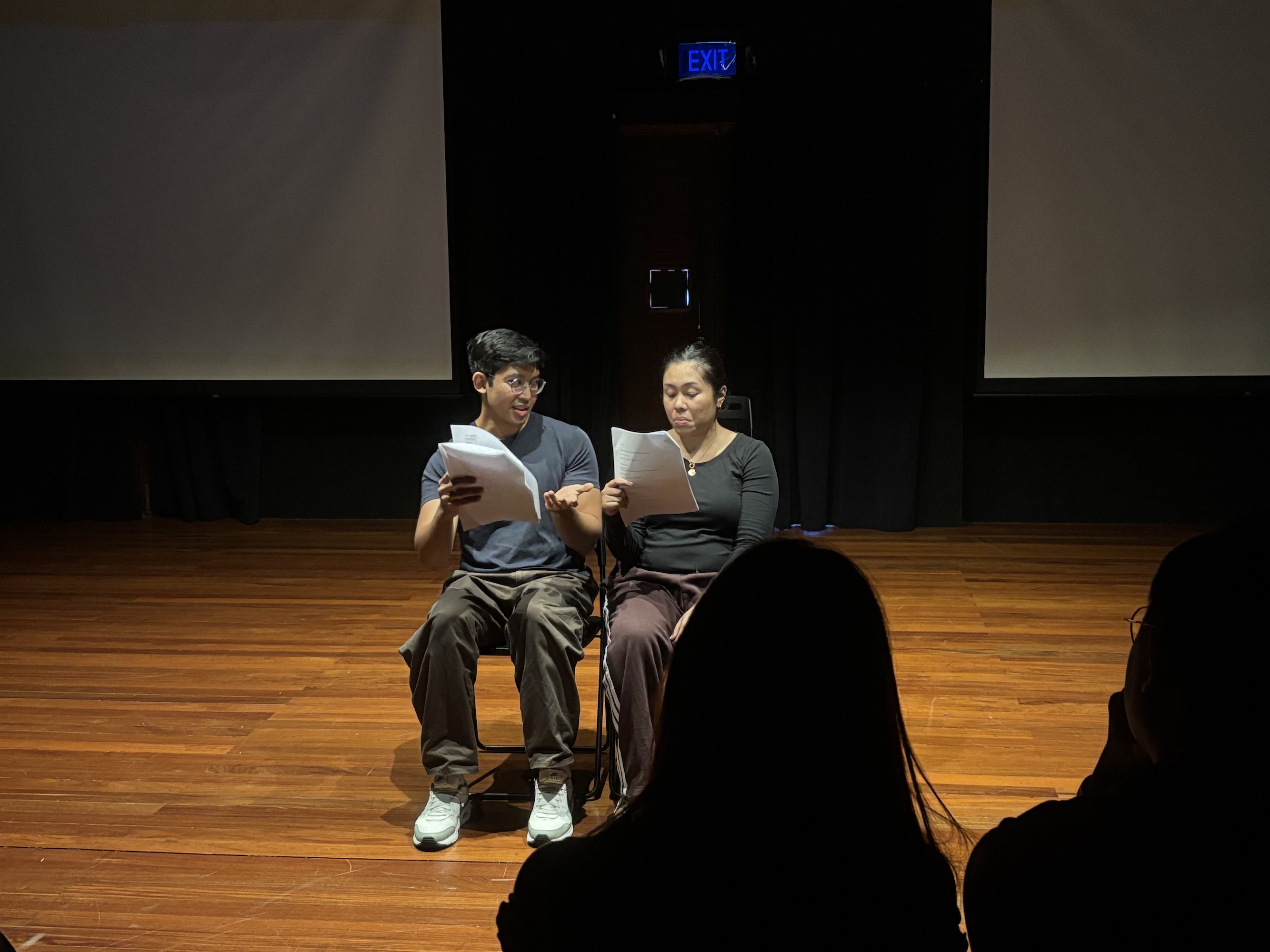 Two persons seated very close to each other on chairs in a black box. Two persons seated very close to each other on chairs in a black box.