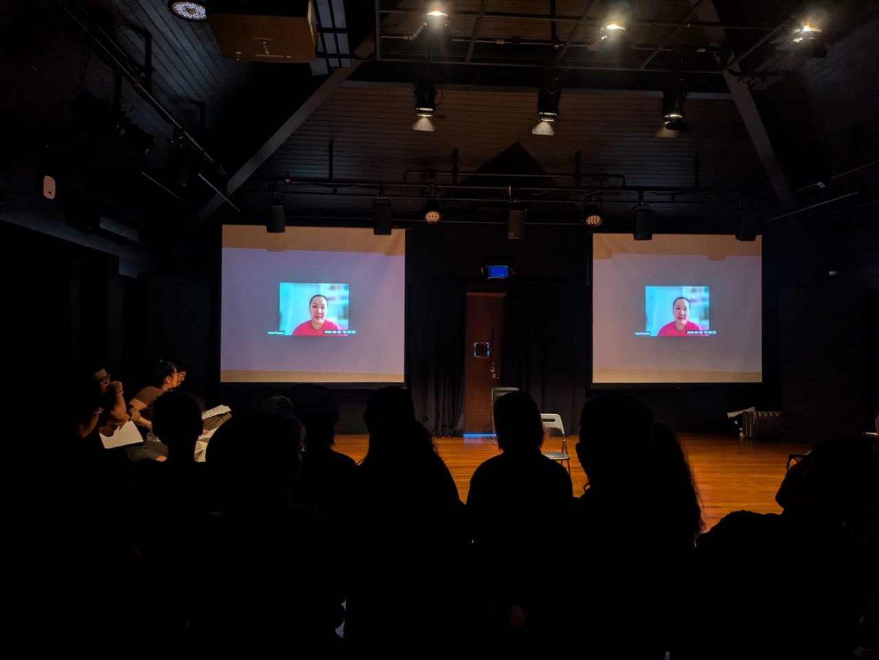 A video featuring a female-presenting person presented on two screens in a black box. A video featuring a female-presenting person presented on two screens in a black box.