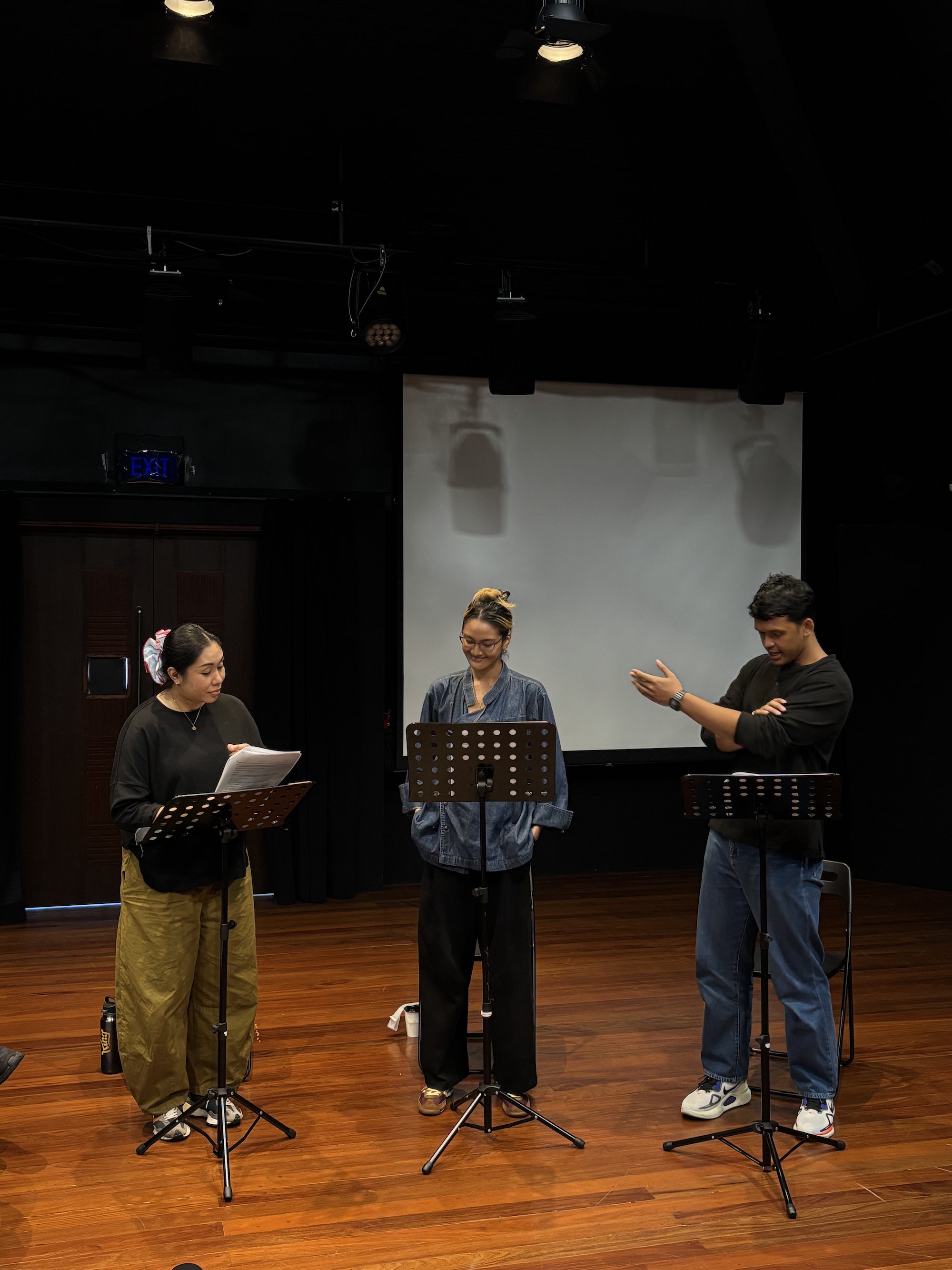 Three persons standing behind music stands, speaking to one another.