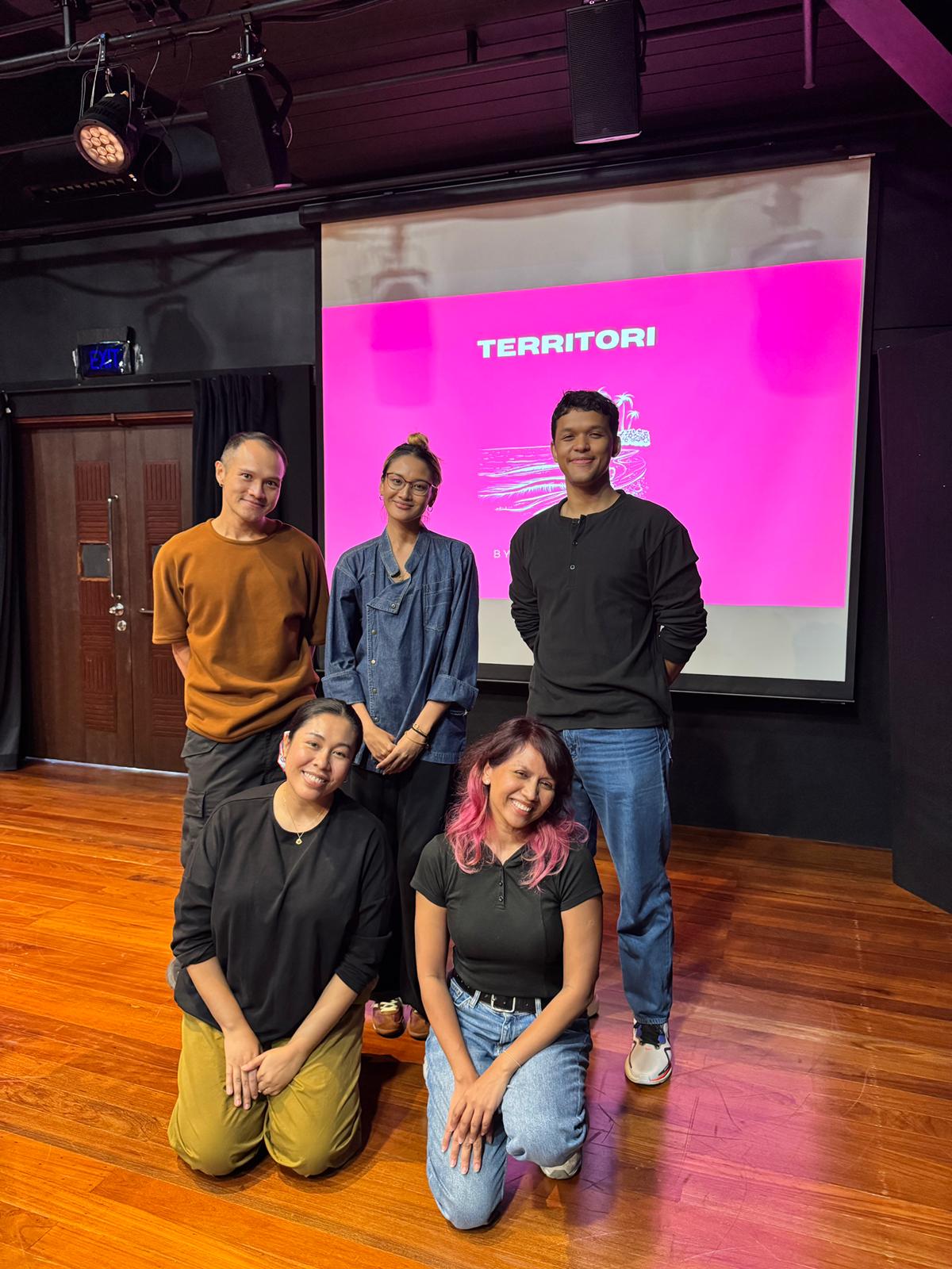 Five people standing and kneeling in a group photo, smiling.