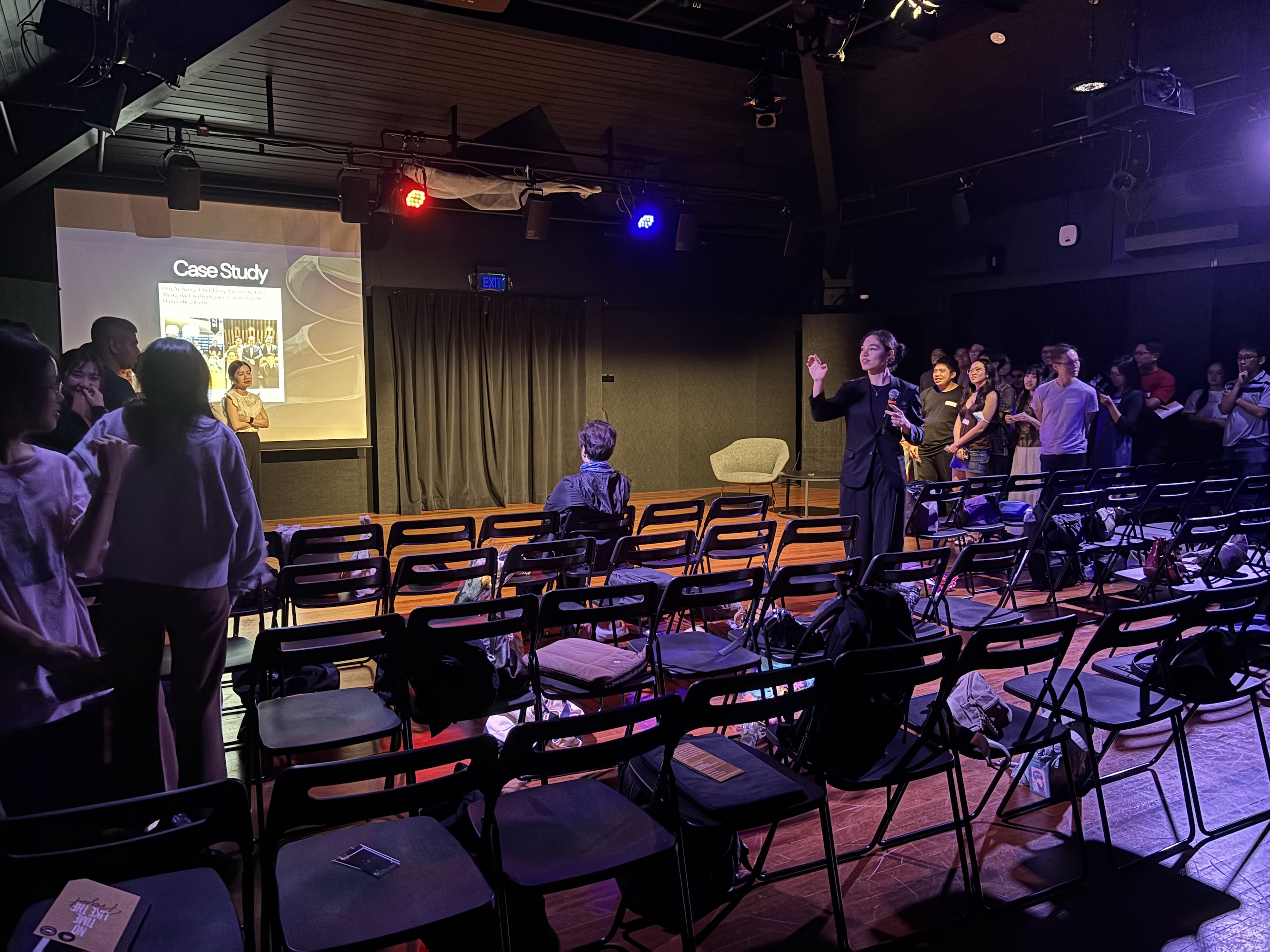 Two groups of people standing on either side of a black box theatre. A female-presenting person is in the middle counting them.