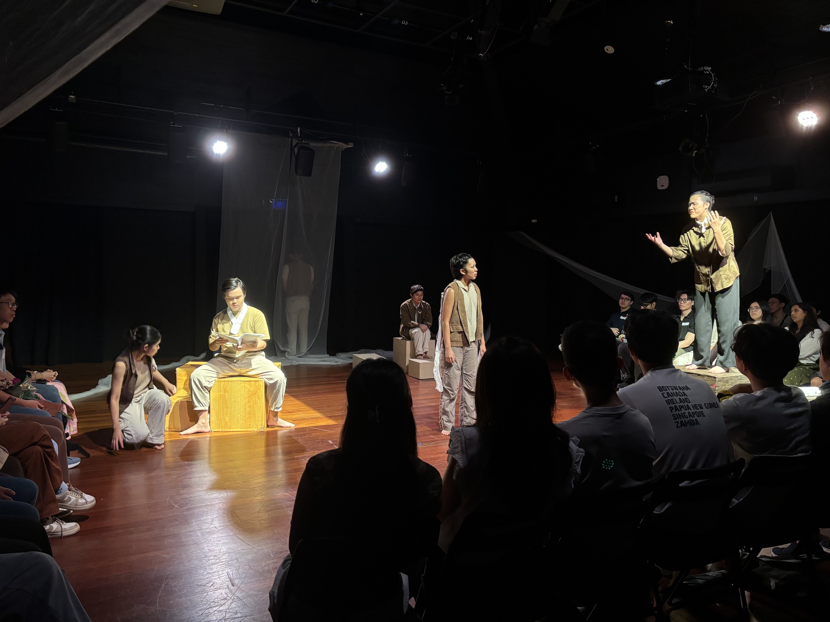 Three people in a Black Box, lit by spotlights, dressed in beige and brown clothes.
