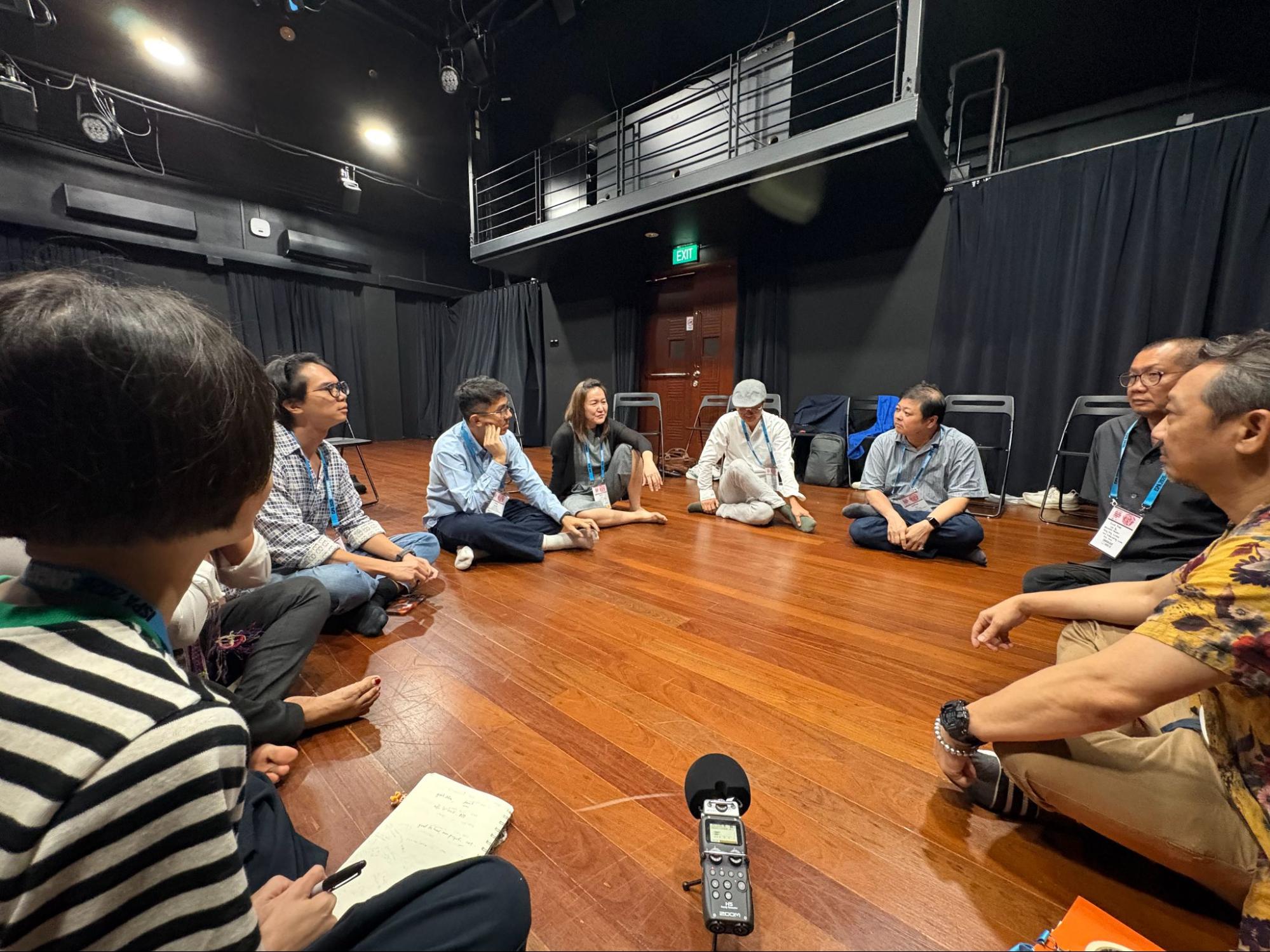 A small group of people seated on the floor in a circle. A small group of people seated on the floor in a circle.