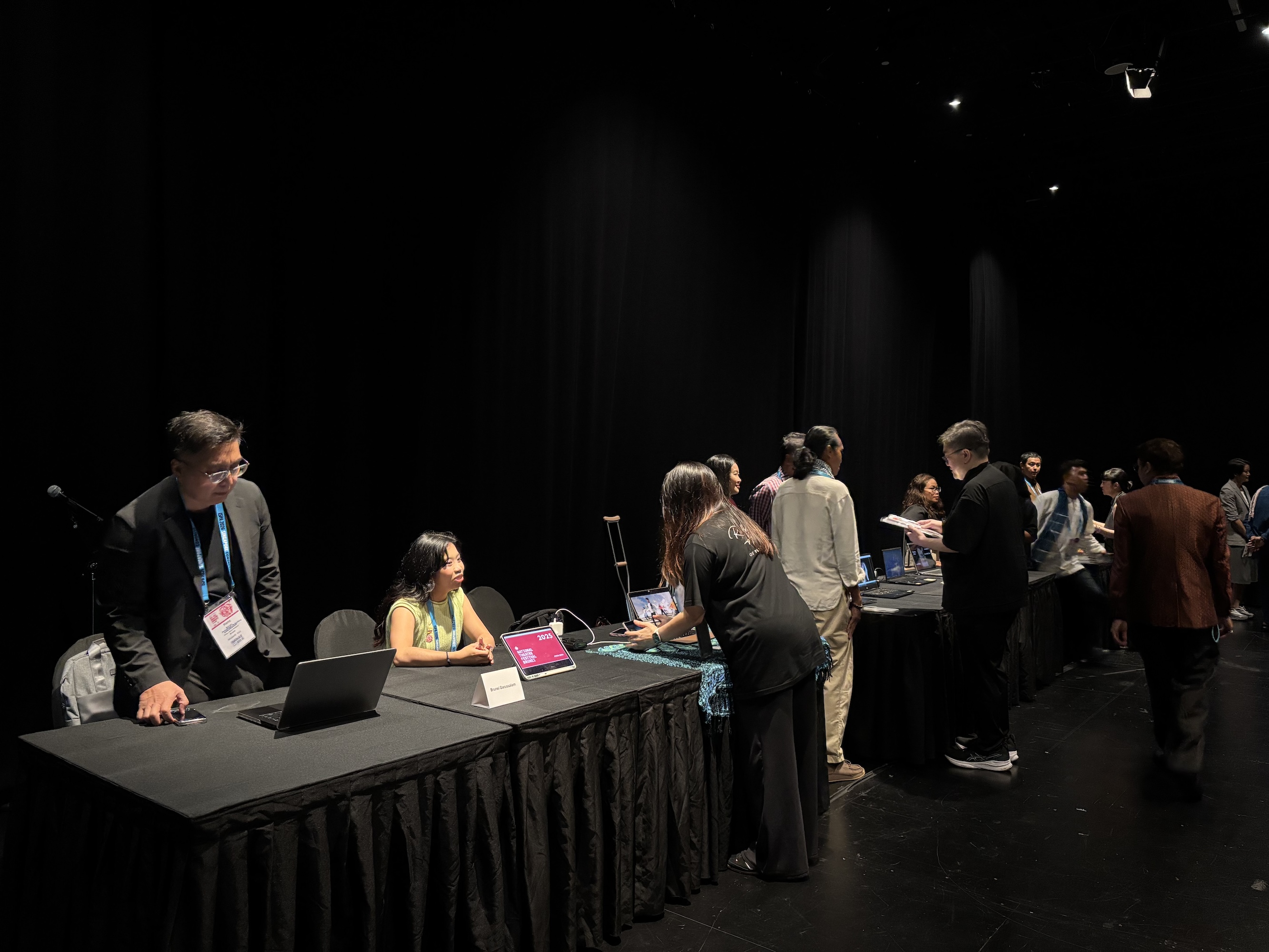 A handful of people seated behind black tables, speaking to people who come by.