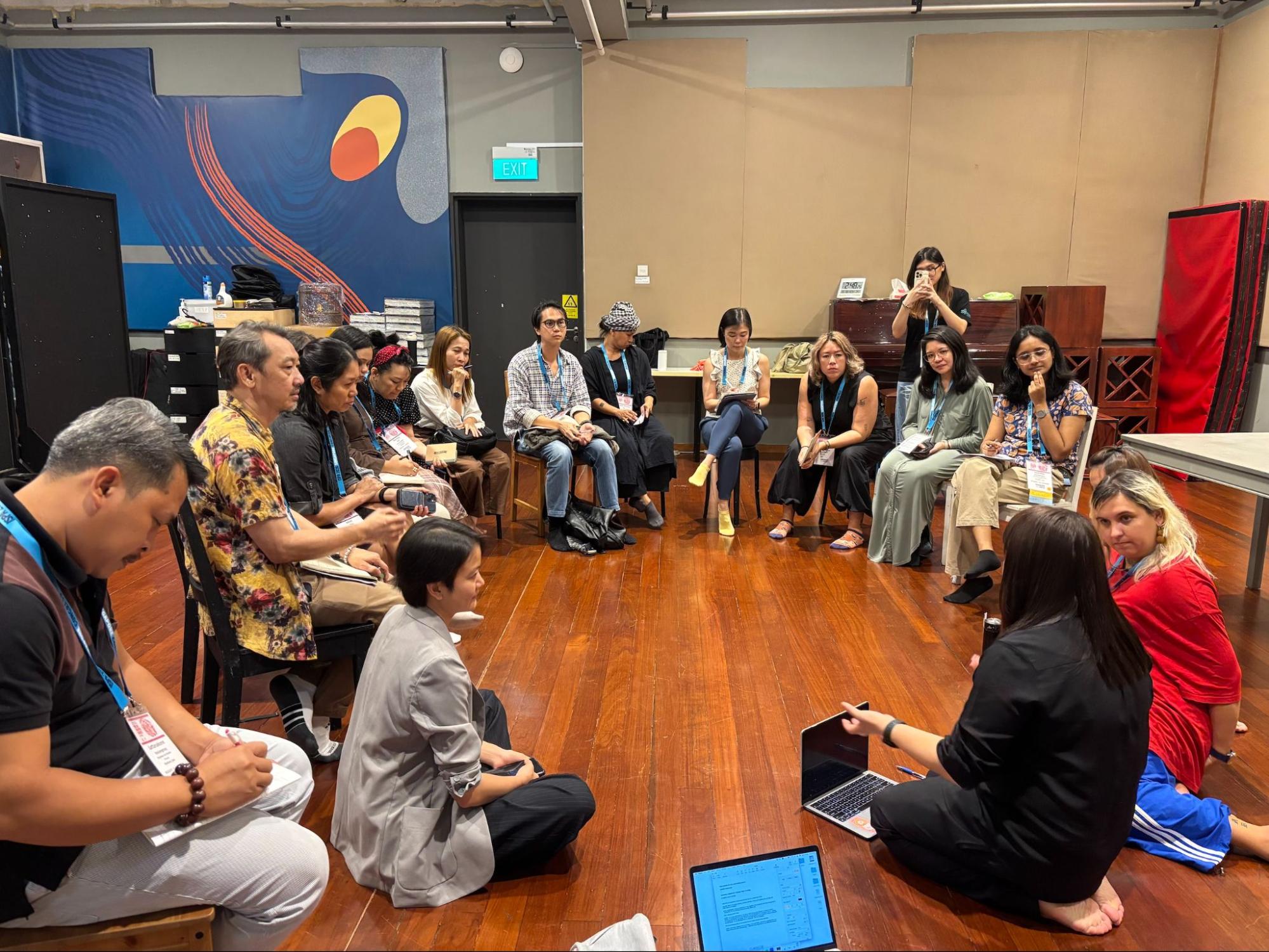 A large group of people seated in a circle, speaking to each other.