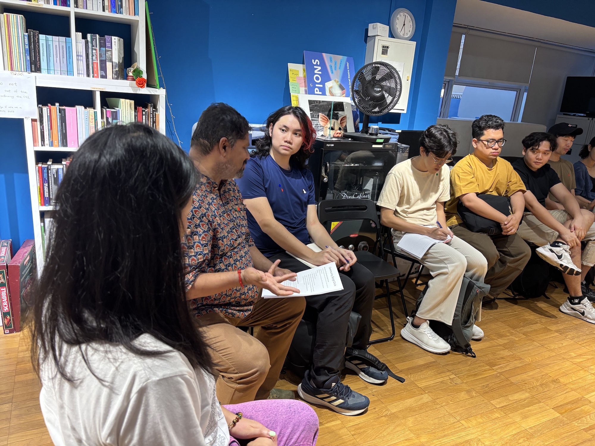 Several people seated in chairs as part of a larger circle, talking.