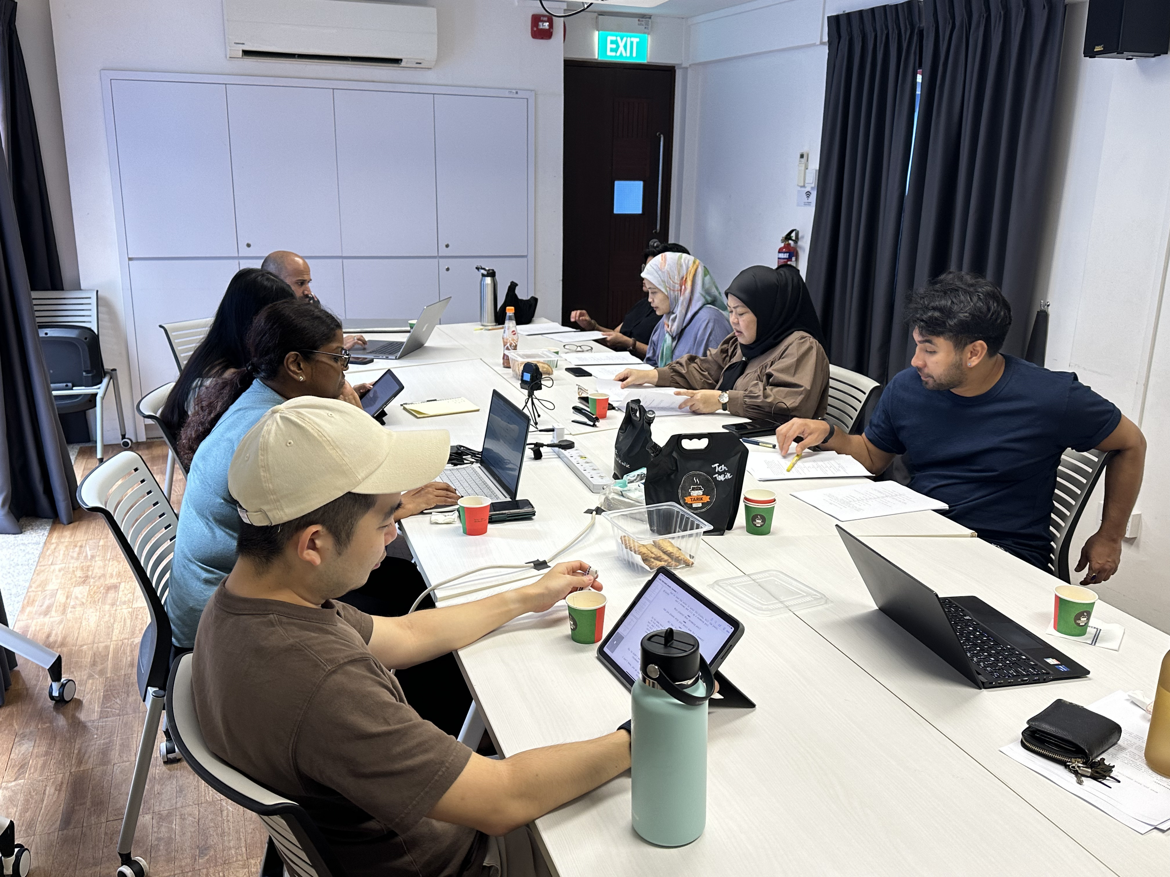 A photo where 8 people are seen gathered around the table with scripts in front of them.